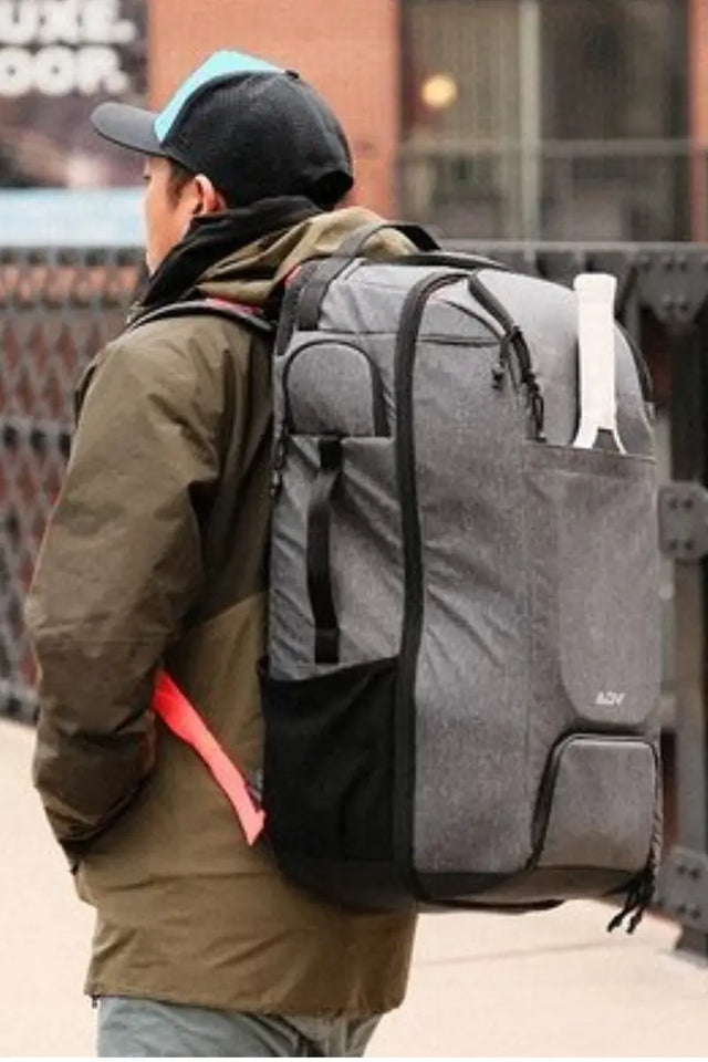 Man wearing a cap and jacket carrying a large tennis travel backpack outdoors