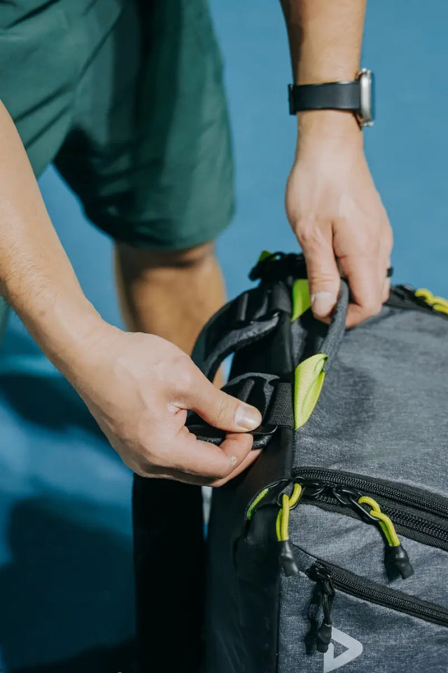 Close-up of hands adjusting the top strap of a gray tennis gear backpack.