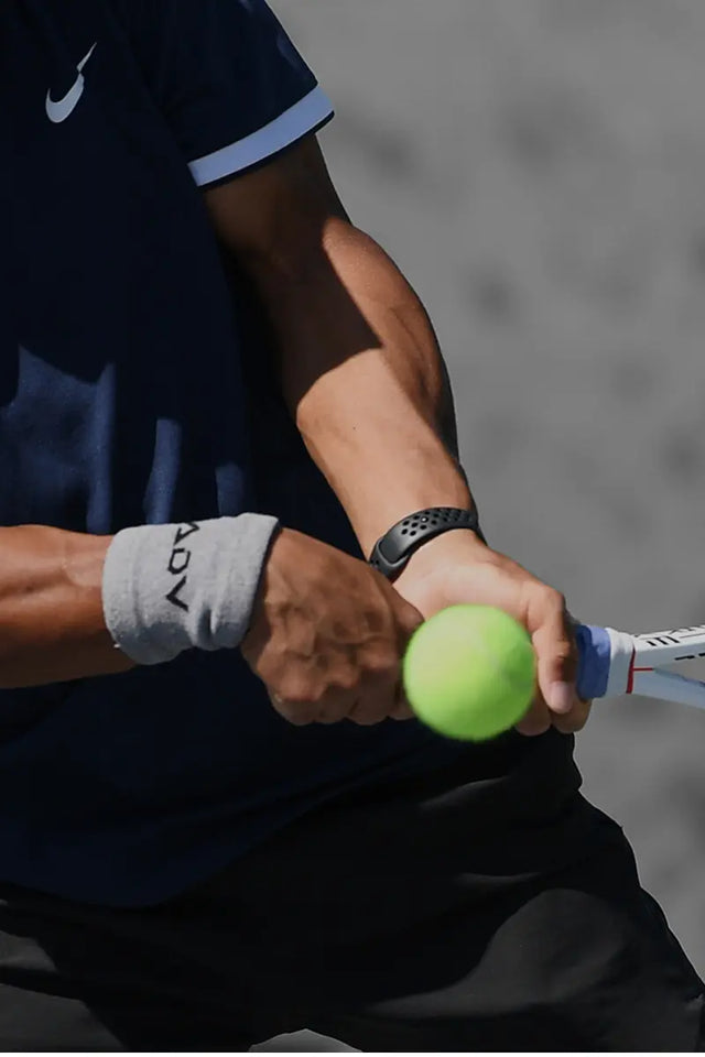 Tennis overgrips on a player's racket handle during a backhand swing with a bright green tennis ball in focus