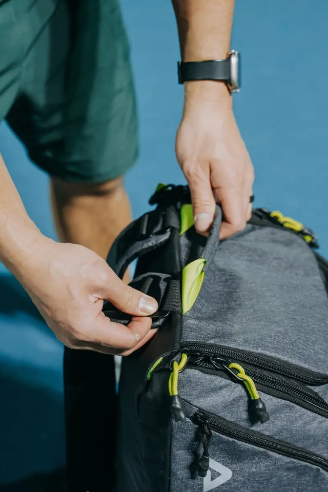 Close-up of hands adjusting straps on a tennis racket bag with bright green details