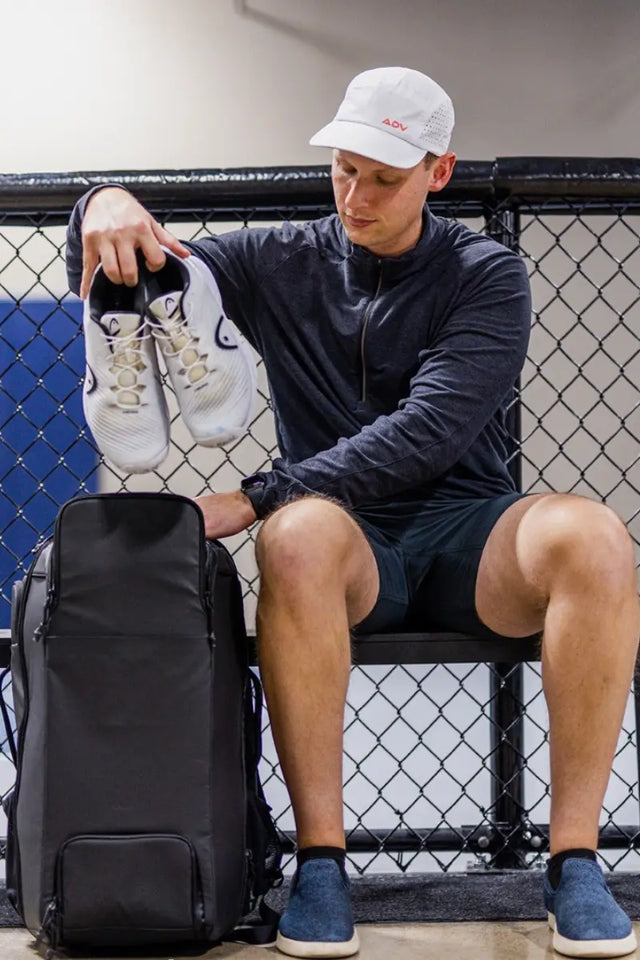 Pickleball Gear packed into a gym bag by a man holding a pair of athletic shoes.