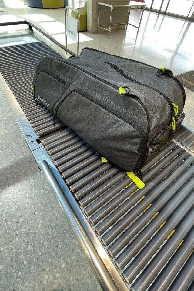 Gray ADV tennis duffel bag on an airport conveyor belt awaiting security scanning.