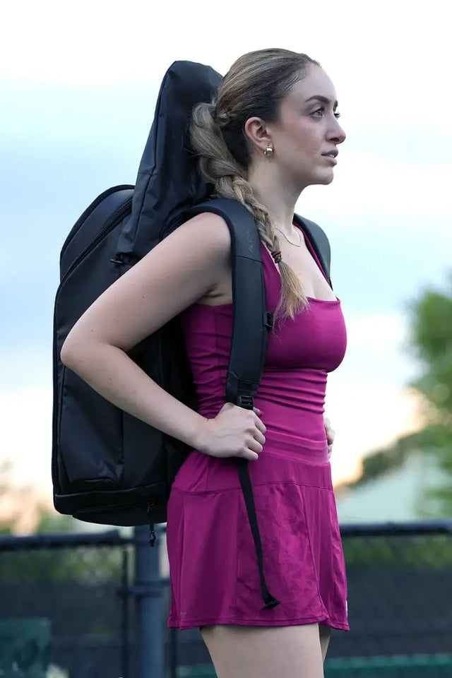 best tennis bag carried by a female player in a magenta outfit, featuring a sleek black design with ample storage for rackets