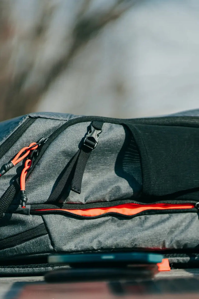 Long-lasting tennis bag with durable zippers, black straps, and bright orange accents in an outdoor setting.