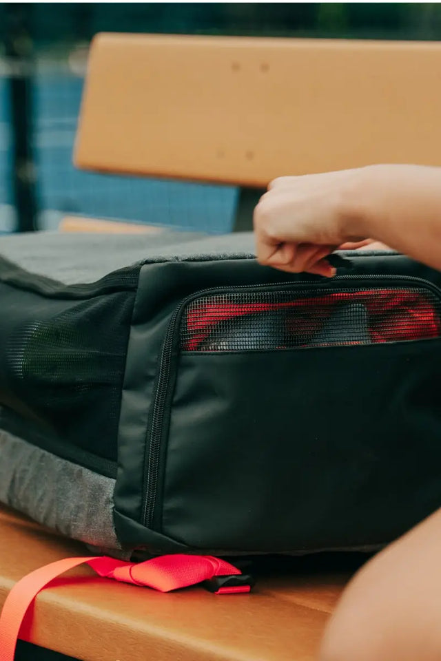 Pickleball bag with red straps being unzipped on a wooden bench, ideal for carrying court essentials