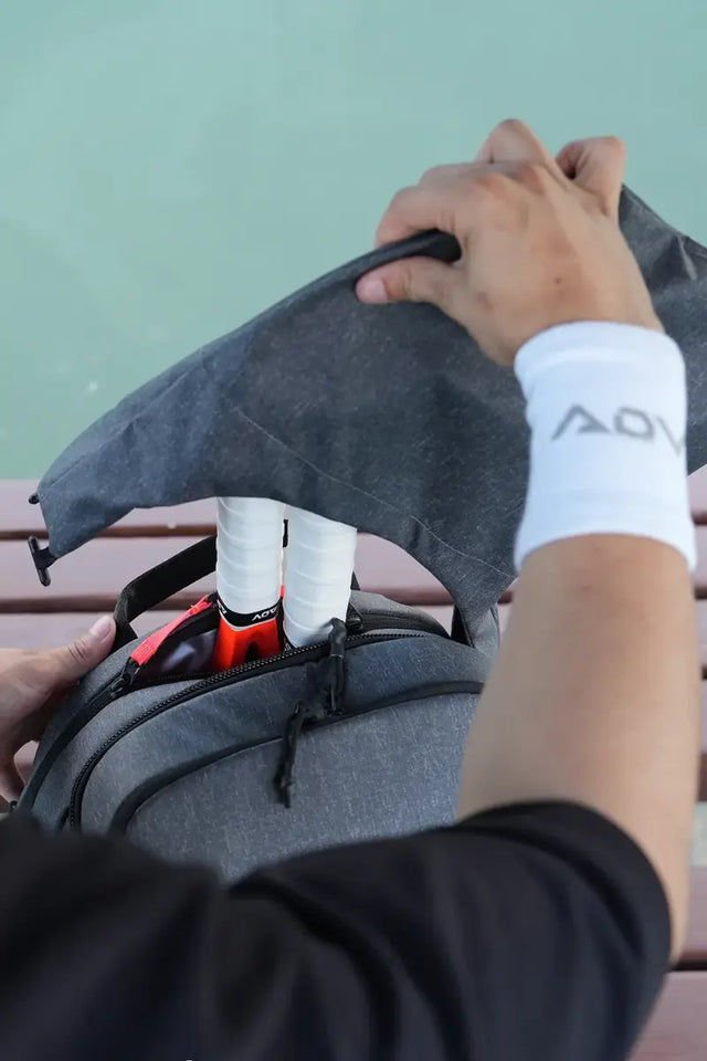 tacky tennis overgrip in blue being wrapped around a racket handle by a focused female player wearing a white wristband