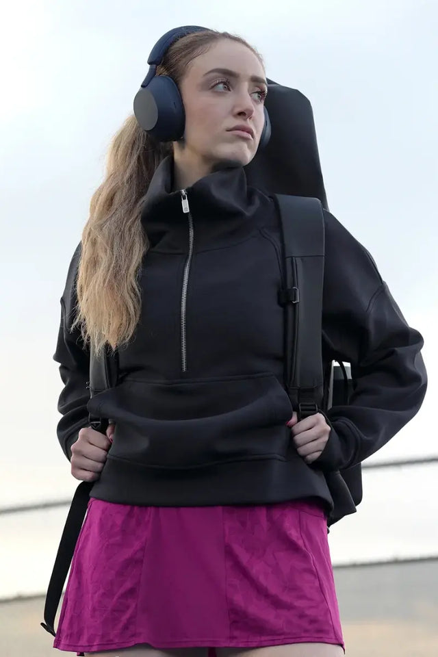 A woman wearing headphones and carrying a tennis backpack looks focused, showcasing essential tennis gear for athletes on the go.