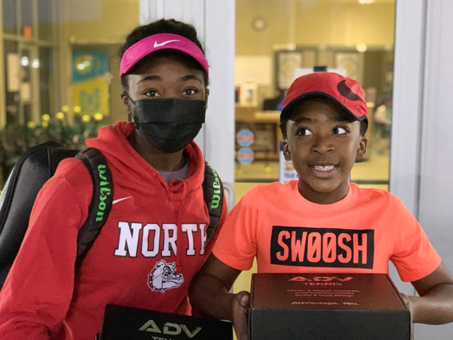 Tennis racket backpack worn by a young athlete standing with a child holding an ADV Tennis box.
