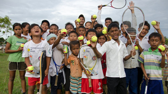 Group of children holding tennis rackets and balls, celebrating outdoors with a pickle ball bag in the background.