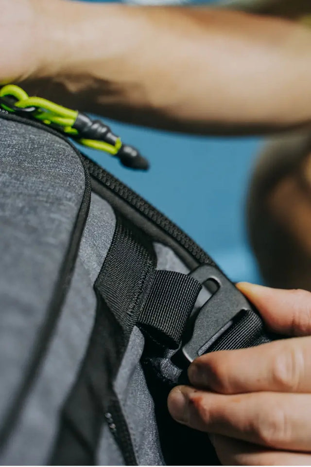 Durable tennis bag being adjusted with a secure strap and zipper featuring bright green detailing.