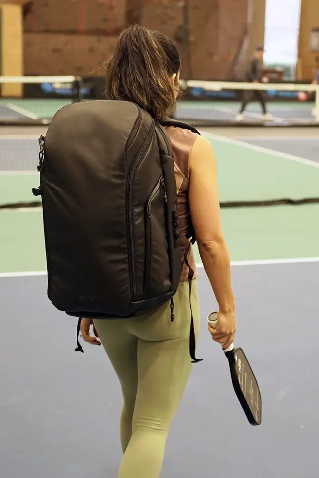 A woman carrying the best pickleball bag walks onto an indoor court, holding a paddle and ready to play.