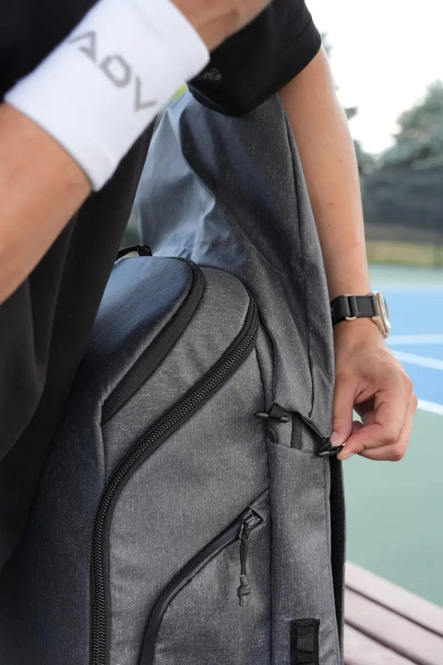 Lightweight tennis bag in gray being zipped by a player near an outdoor court