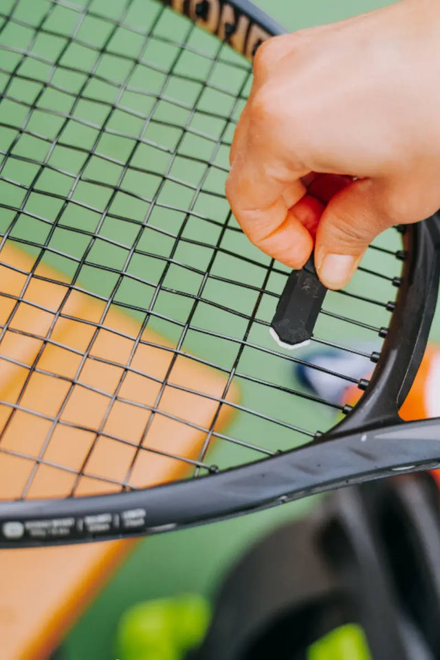 Tennis racket dampener being installed on the black racket strings to reduce vibration during play.