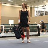 Tennis racquet bag carried by a player on an indoor court, featuring a sleek design with multiple compartments and red accents.